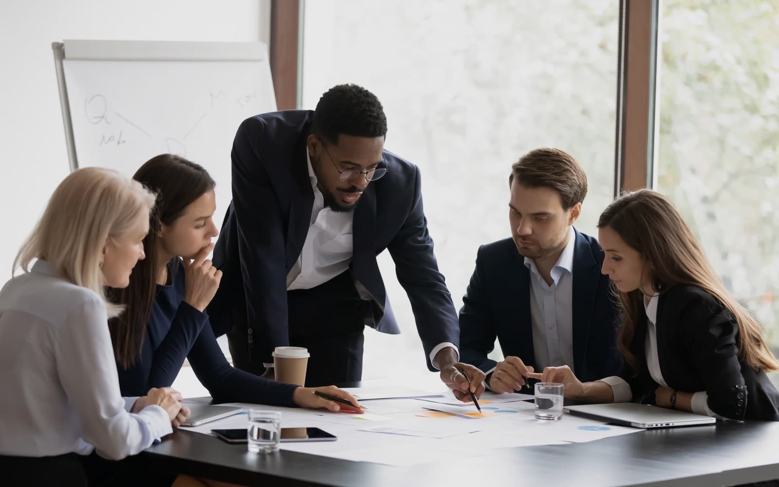 Five colleagues around a boardroom table, one standing and pointing at the charts in front of them