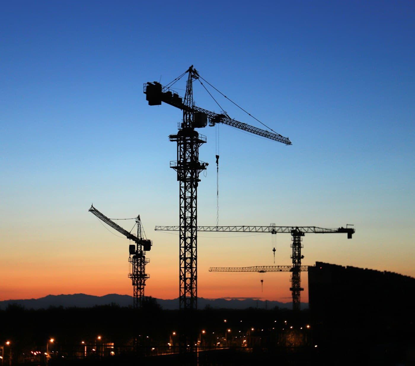 Tower cranes silhouetted over a building site at dusk
